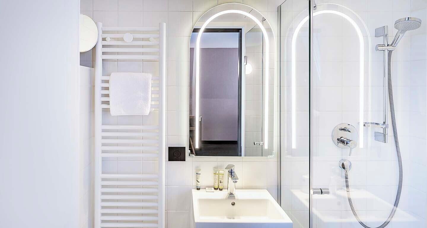 Un baño moderno con ducha de vidrio, lavamanos blanco y espejo con iluminación integrada.