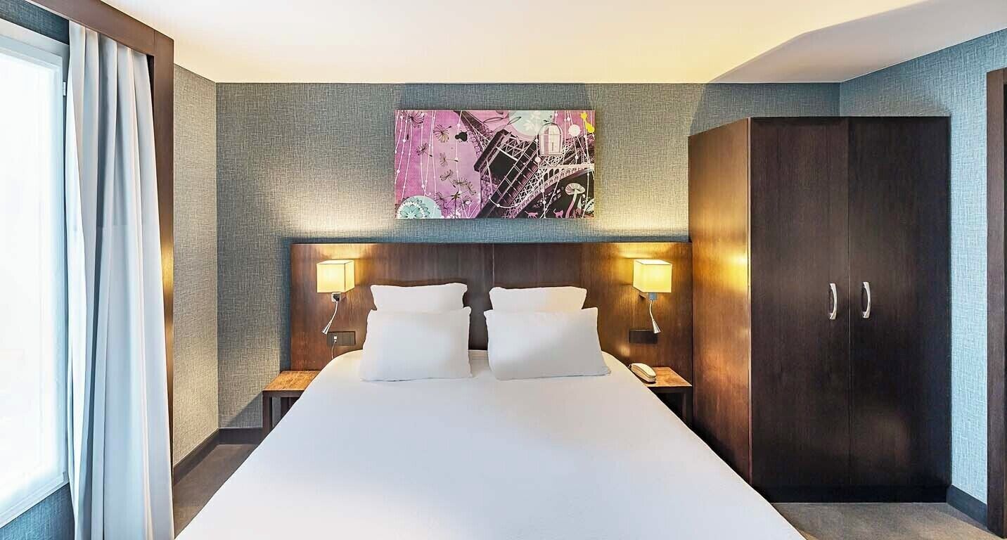 Une chambre d’hôtel avec un grand lit, deux lampes de chevet, une tête de lit ornée d’une œuvre d’art fixée au mur et une armoire.
