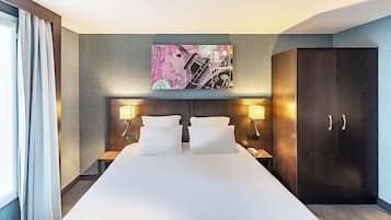 Une chambre d’hôtel avec un grand lit, deux lampes de chevet, une tête de lit ornée d’une œuvre d’art fixée au mur et une armoire.