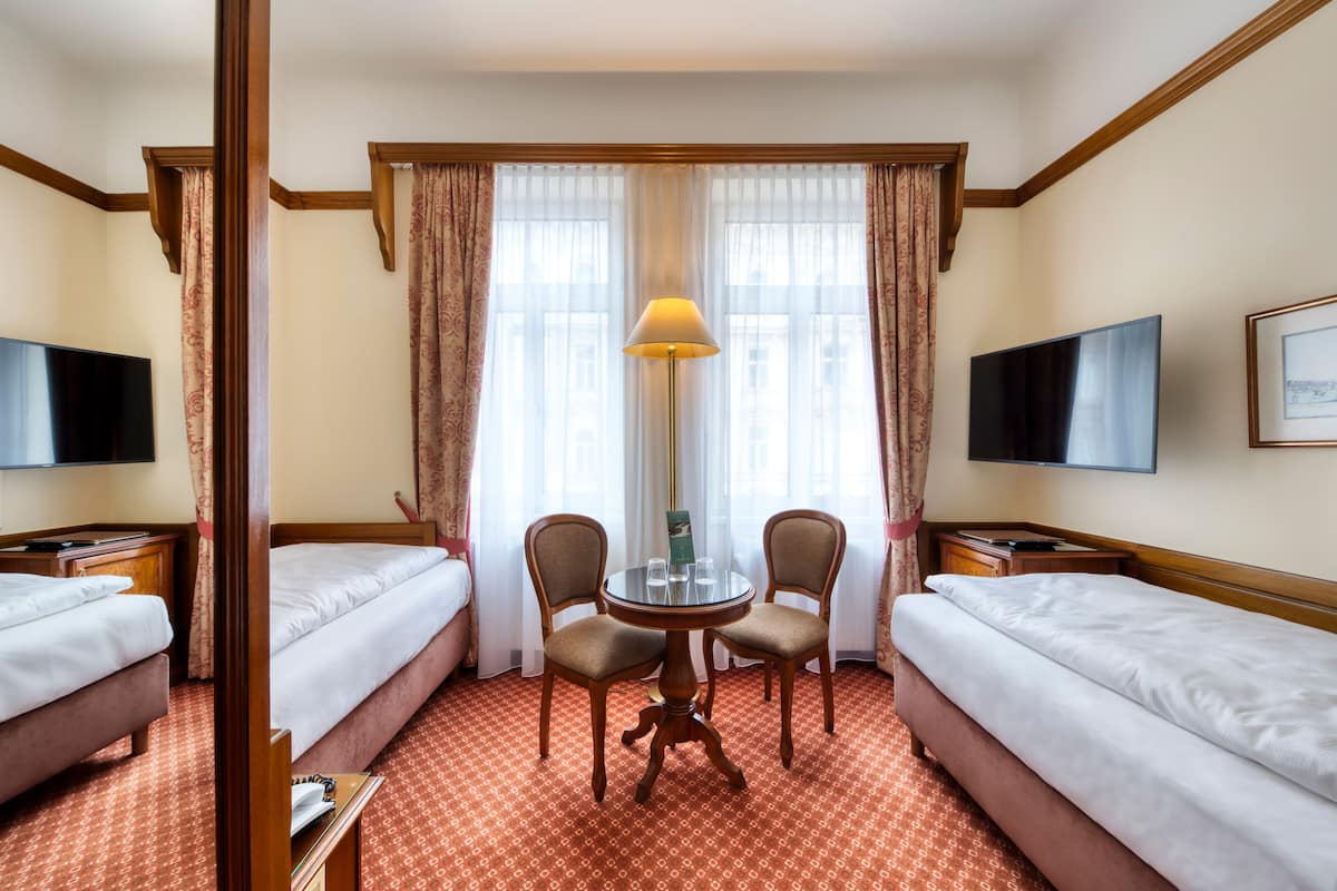 A hotel room with two beds, a round table with chairs, a lamp, a TV, and a framed picture on the wall.