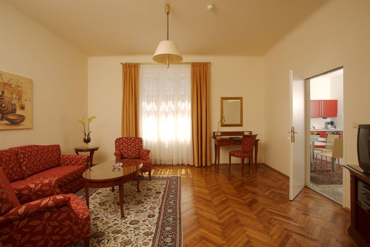 A living room with a sofa, armchair, coffee table, and a dining area with a table and chairs. There is a television and a mirror on the wall.