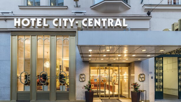 The entrance of Hotel City-Central with a large glass door, a sign above, and two potted plants. - Hotel City Central (Vienna)