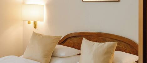Una cama bien hecha con ropa de cama blanca y un cabecero de madera, una lámpara de pared y un cuadro en la pared.