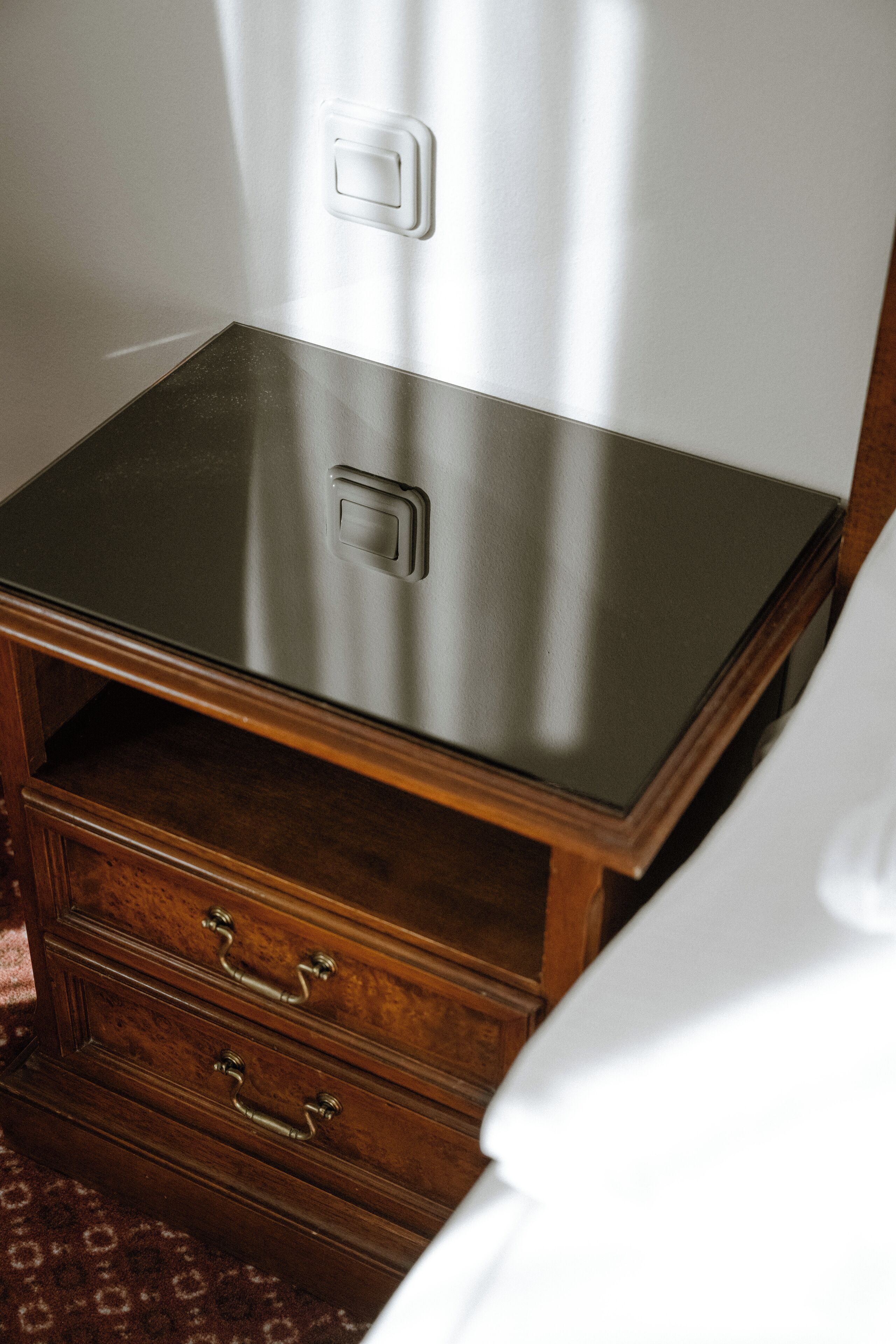 A wooden nightstand with drawers and a switch on the wall.