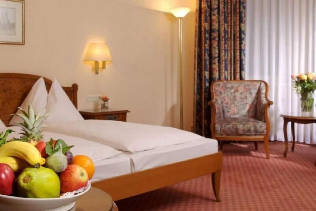 A hotel room with a bed, a chair, a nightstand, a lamp, and a fruit bowl.