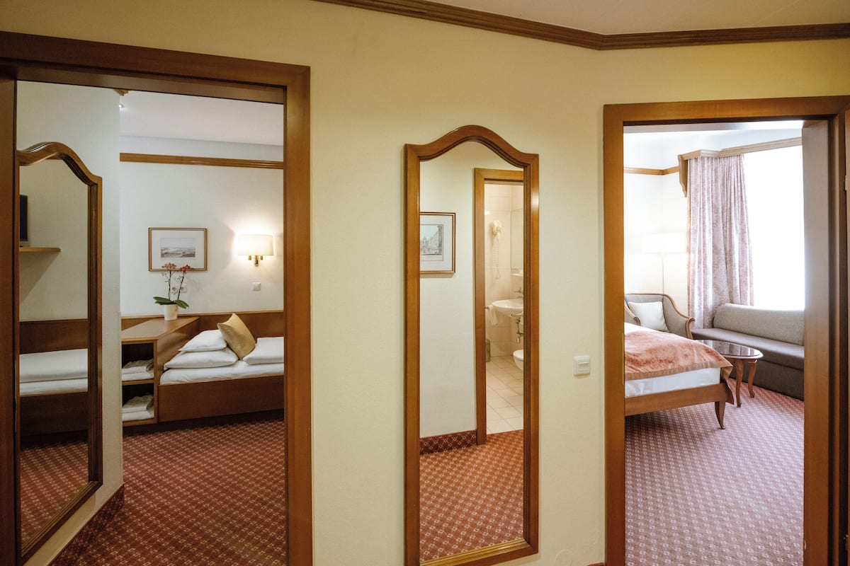 A hotel room with a bed, a sofa, a small table, and a mirror.