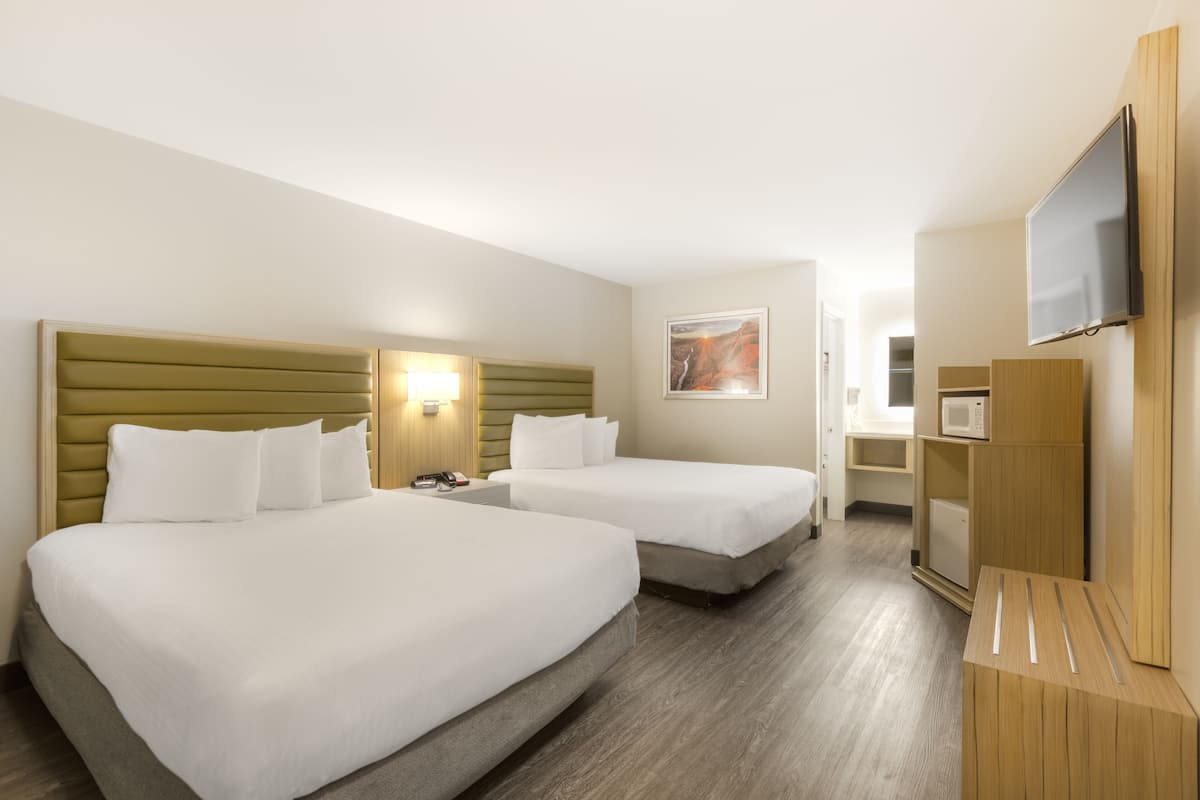 A hotel room with two beds, a flat-screen TV, a microwave, and a small kitchenette.