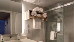A modern bathroom with a glass shower enclosure, a white toilet, a sink with a wooden vanity, and a towel rack with neatly folded towels. - GreenTree Inn Flagstaff (Flagstaff)