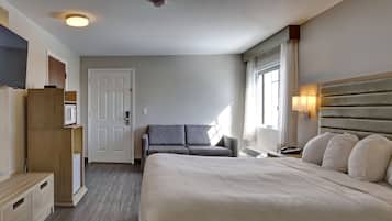 A hotel room with a large bed, a sofa, a TV, a wardrobe, and a window with curtains.
