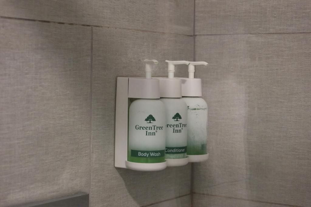 A wall-mounted dispenser with two bottles of GreenTree Inn body wash and conditioner.