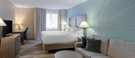 Una habitación de hotel con una cama, un sofá, un escritorio y una televisión.