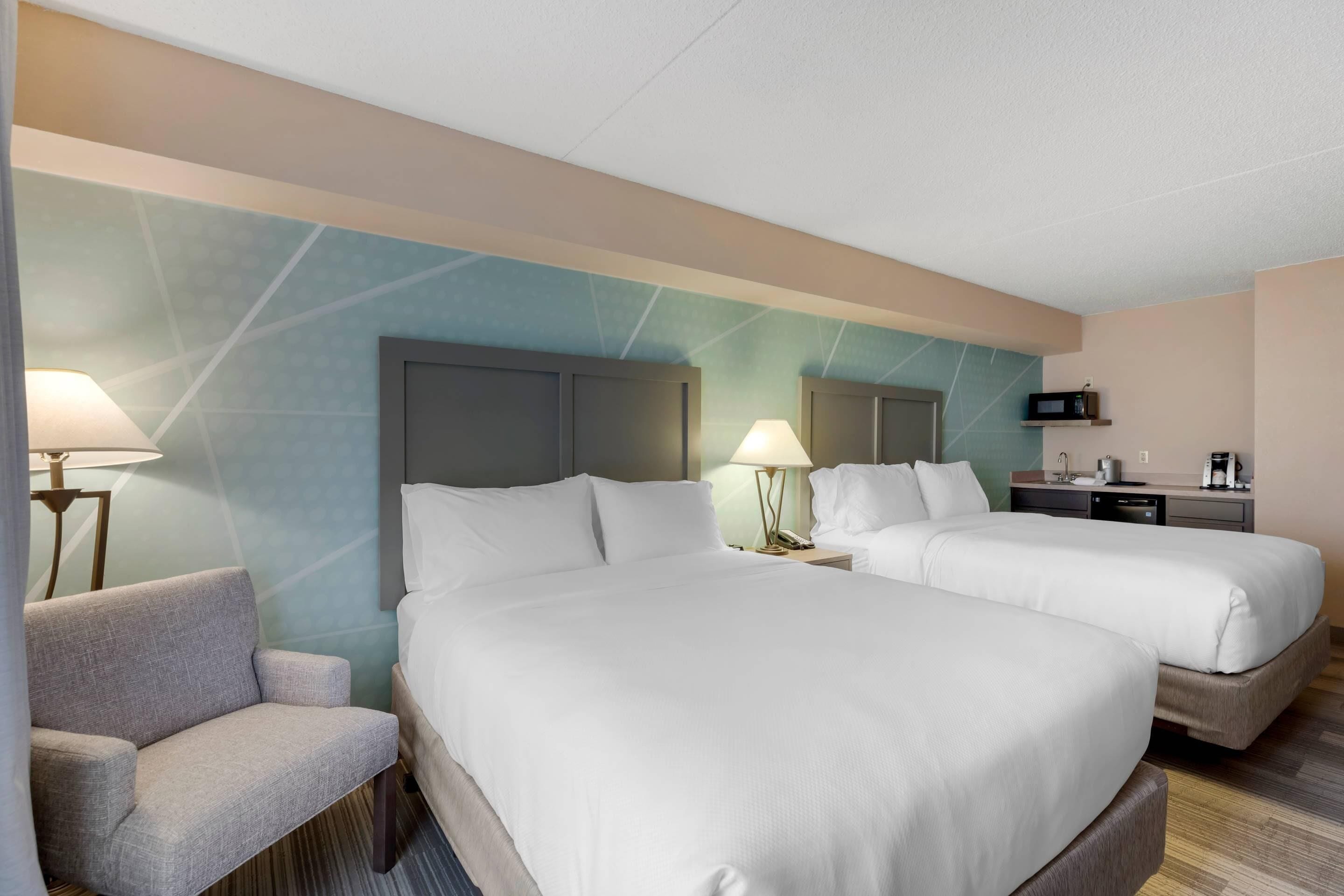 Habitación de hotel con dos camas, un sofá, un escritorio, un microondas y una lámpara.