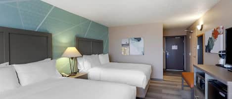 A hotel room with two beds, a desk, a lamp, and a kitchenette.