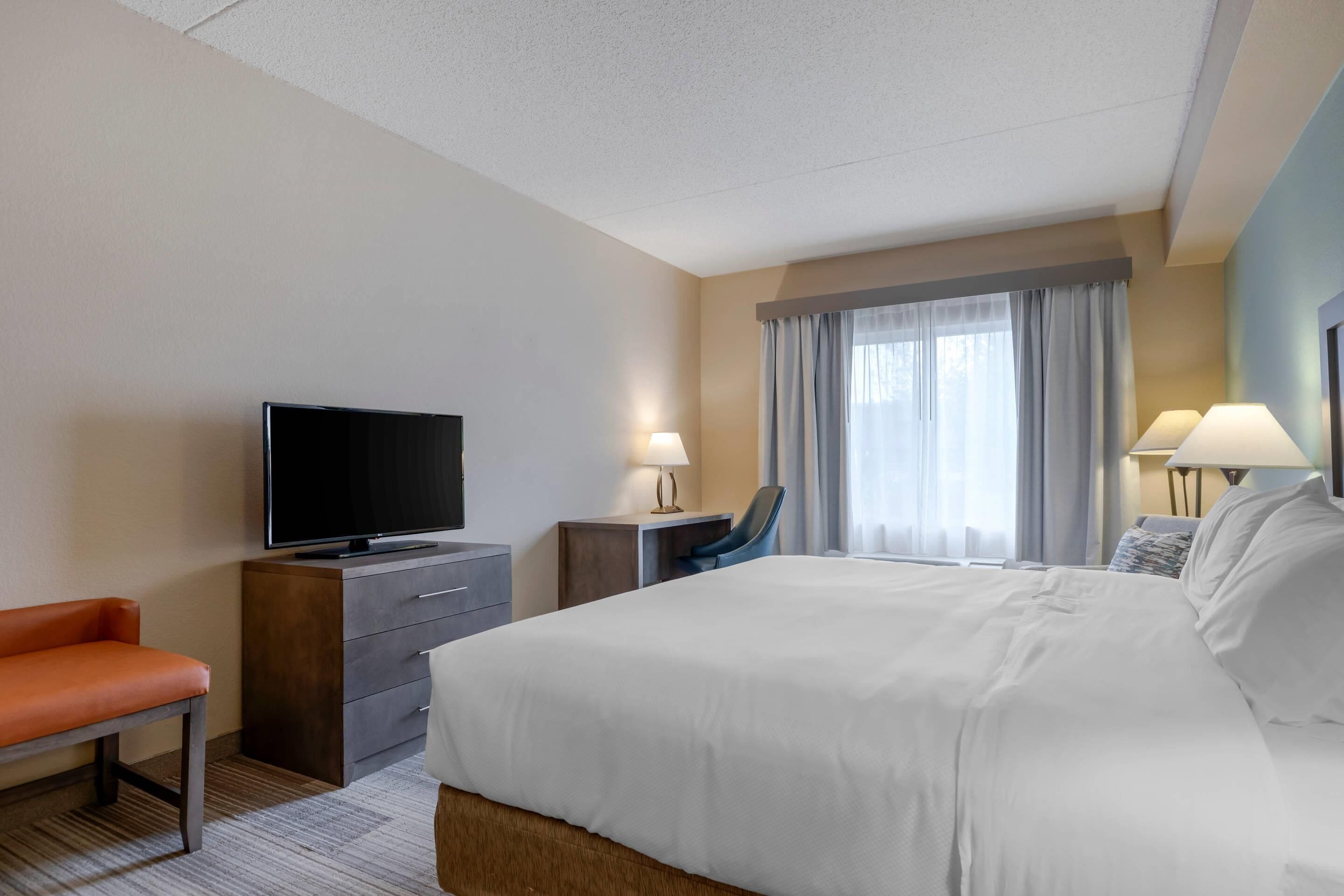 A hotel room with a bed, a television, a desk with a chair, and two lamps.