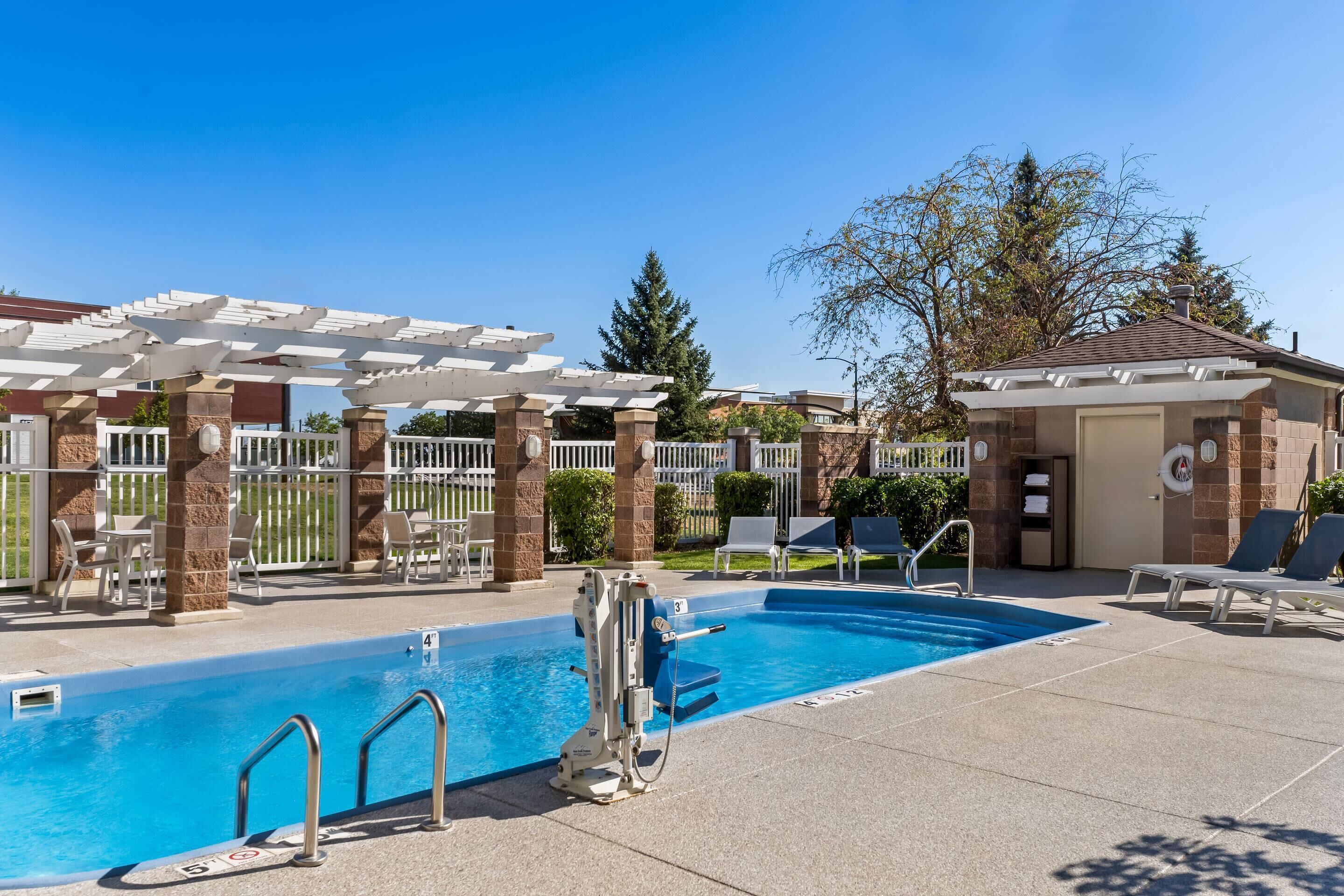 Un área de piscina con una pérgola, sillas de descanso y un puesto de socorristas.