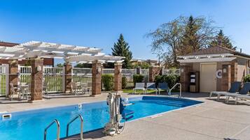 Un área de piscina con una pérgola, sillas de descanso y un puesto de socorristas.