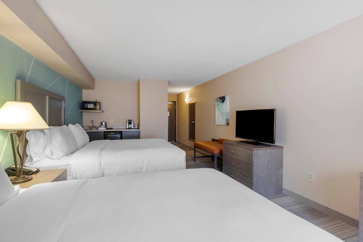 A hotel room with two beds, a desk, a chair, a television, and a microwave.