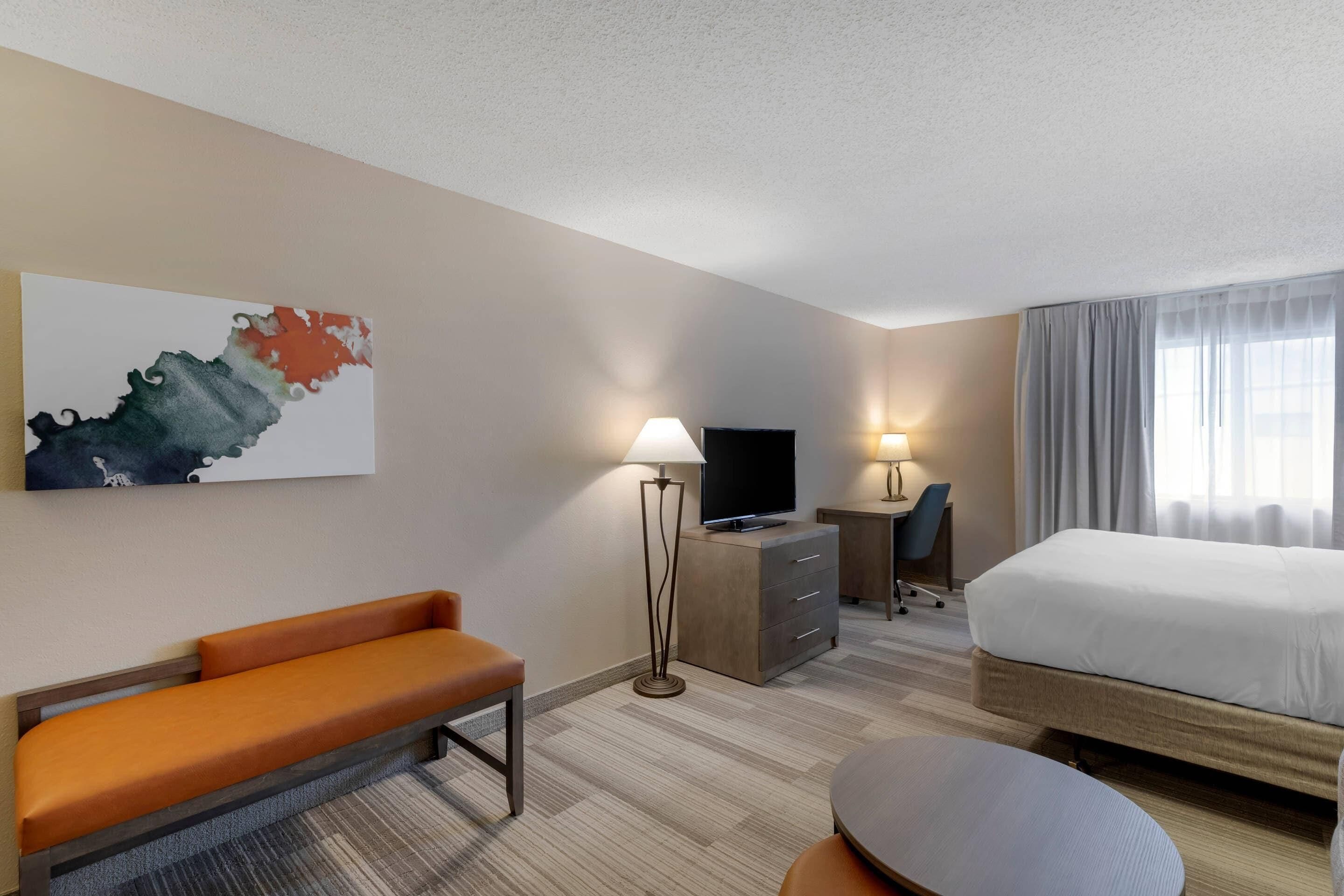 A hotel room with a bed, a desk, a chair, a sofa, and a TV.