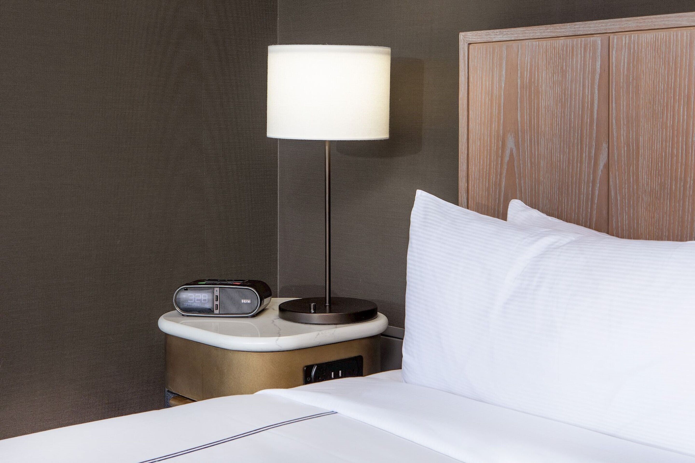 A neatly made bed with white linens, a bedside table with a lamp, and a radio.