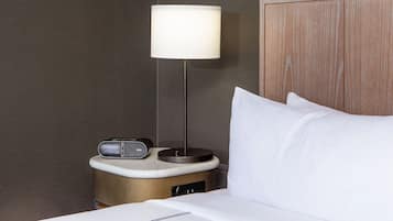 A neatly made bed with white linens, a bedside table with a lamp, and a radio.