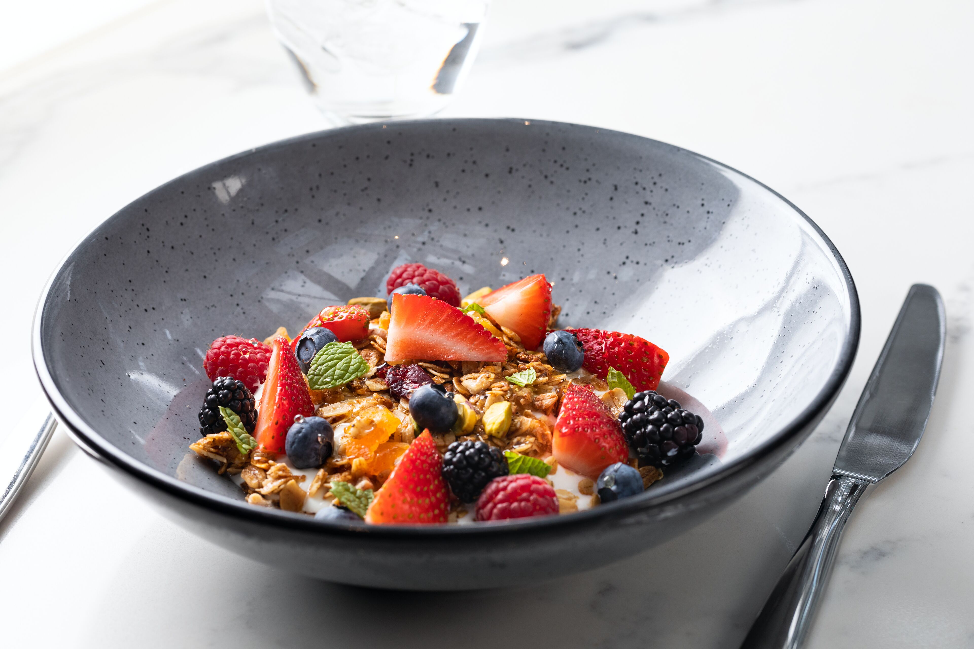 A bowl of cereal with various fruits and granola.