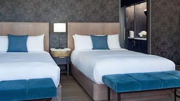 Une chambre d’hôtel avec deux lits, une table de chevet avec une lampe, un banc et un miroir.