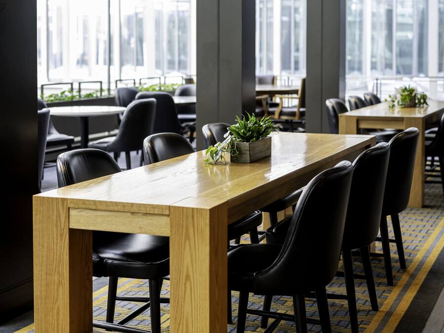 A modern conference room with a long wooden table, black chairs, and a potted plant on the table.