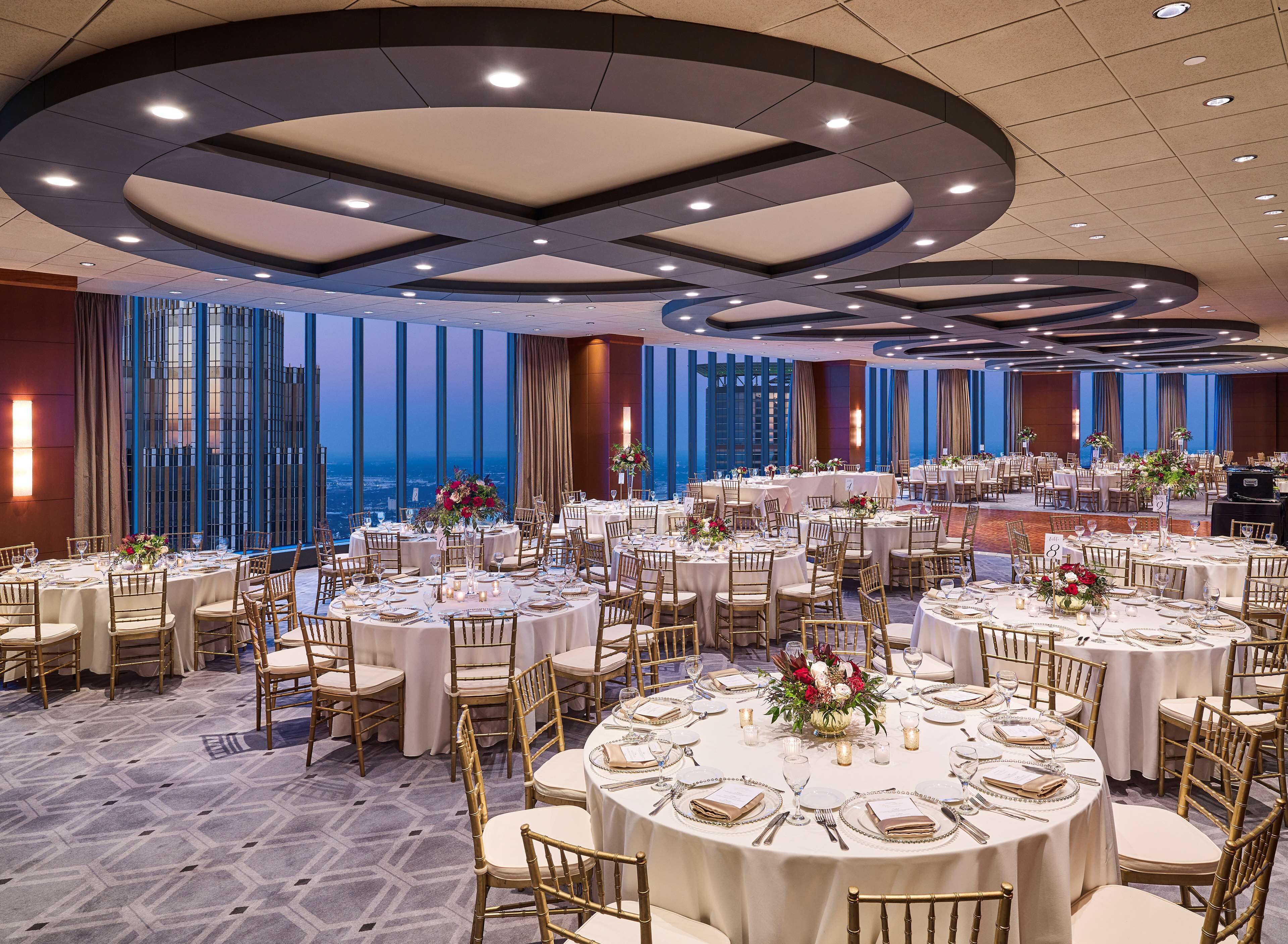 A banquet hall with round tables, gold chairs, and white tablecloths.