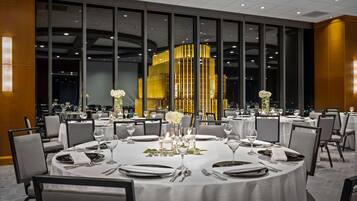 A restaurant with round tables set for dining, large windows, and a view of the city at night.