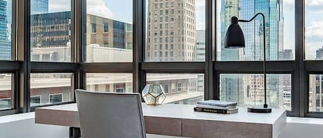 Una oficina moderna con escritorio, silla y lámpara, y ventanas amplias que ofrecen vistas de la ciudad.