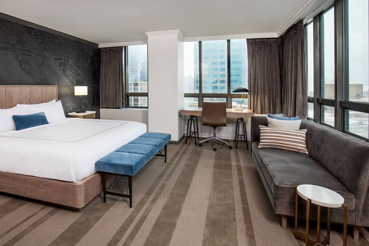 Hotellihuone, jossa on suuri sänky, työpöytä, sohva ja näkymä kaupunkiin.