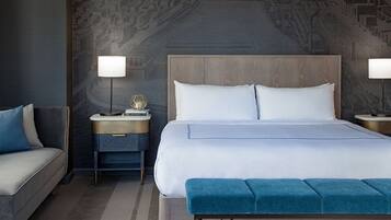 Una habitación de hotel moderna con una cama grande, una mesita de noche con lámpara, un sofá y un papel tapiz estampado.