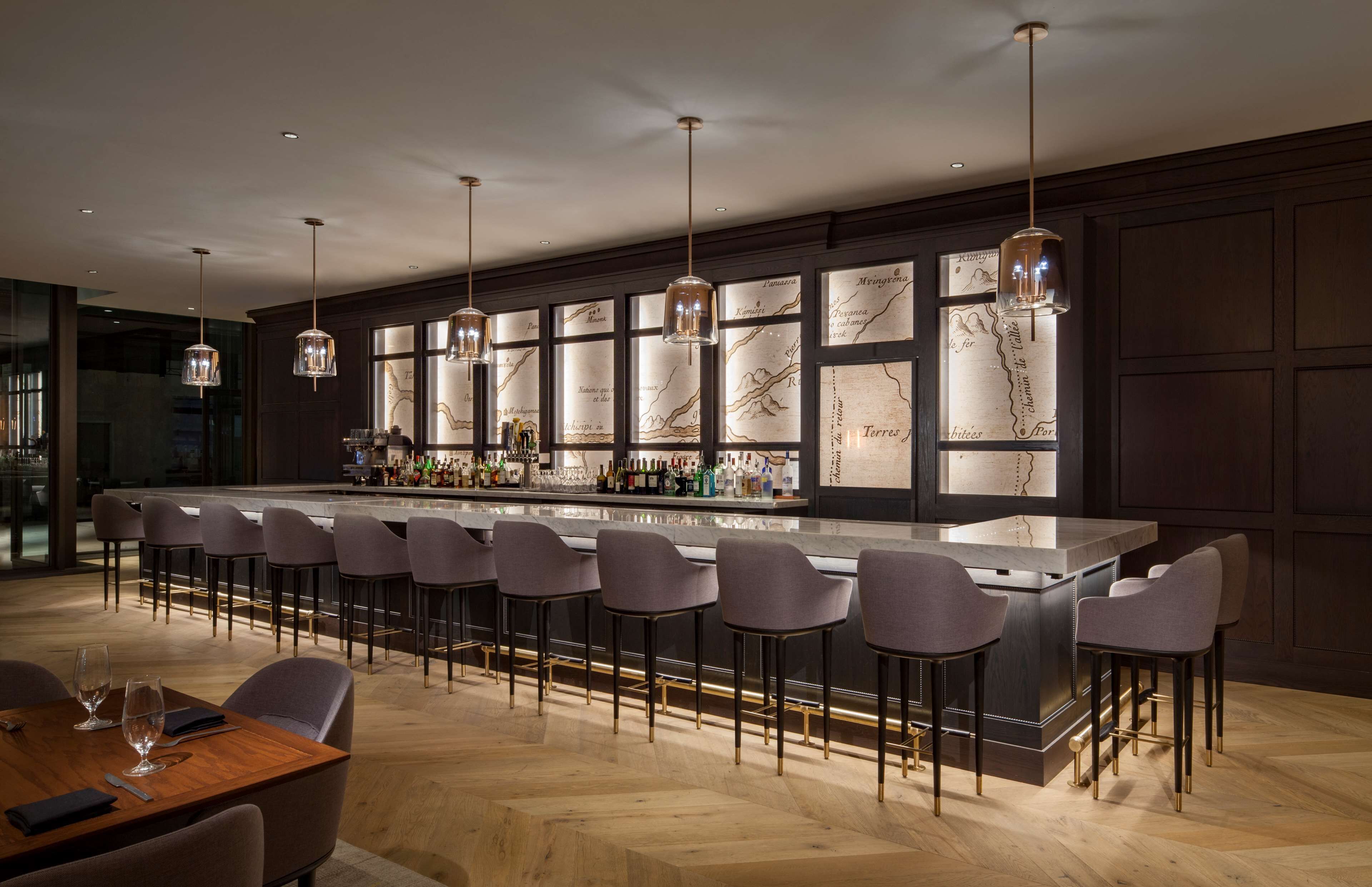 Eine moderne Bar mit einer langen Theke, mehreren Barhocker und hängenden Pendelleuchten.