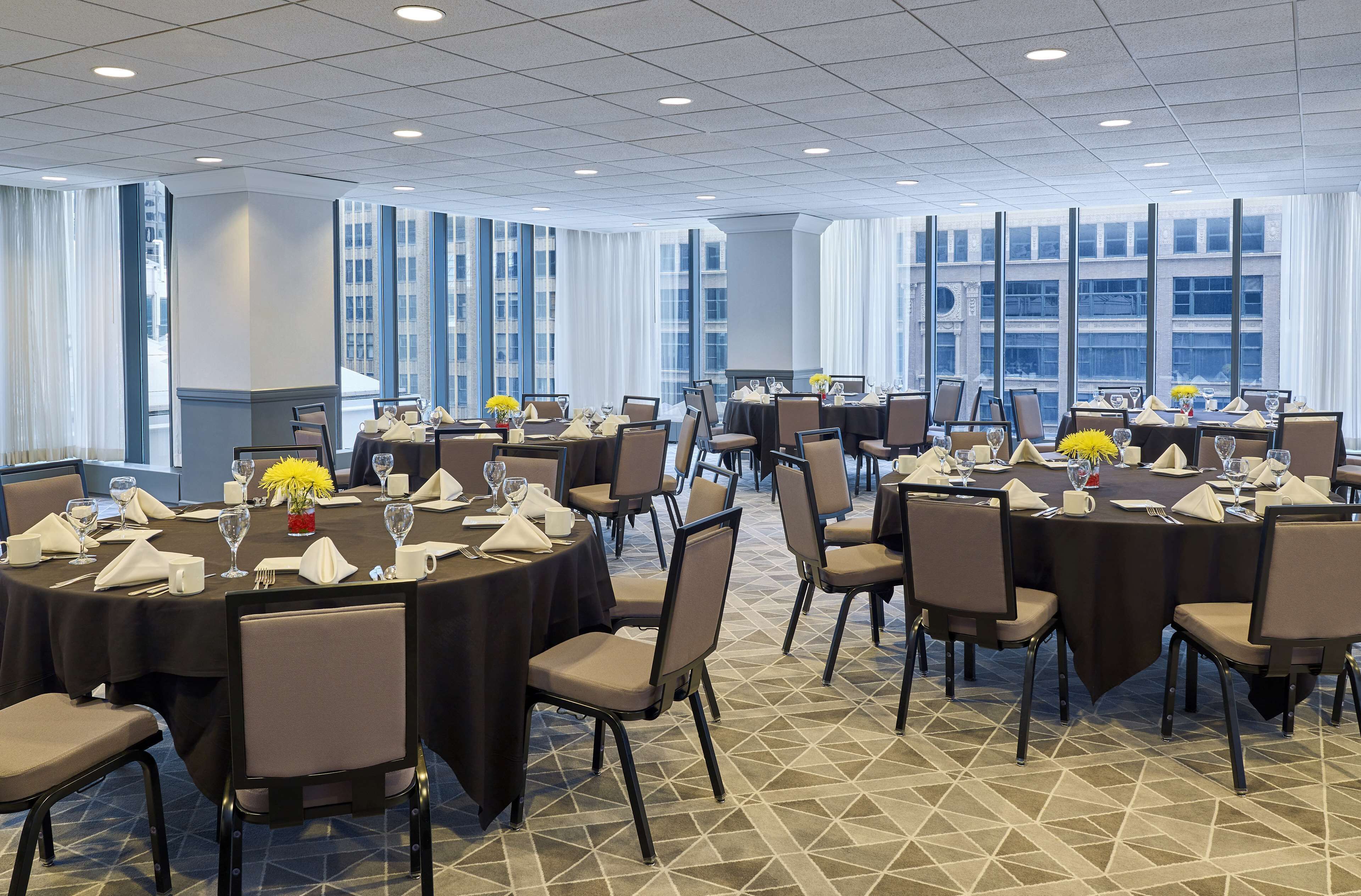 A conference room with multiple round tables, each set with chairs, glasses, and a small vase of yellow flowers.