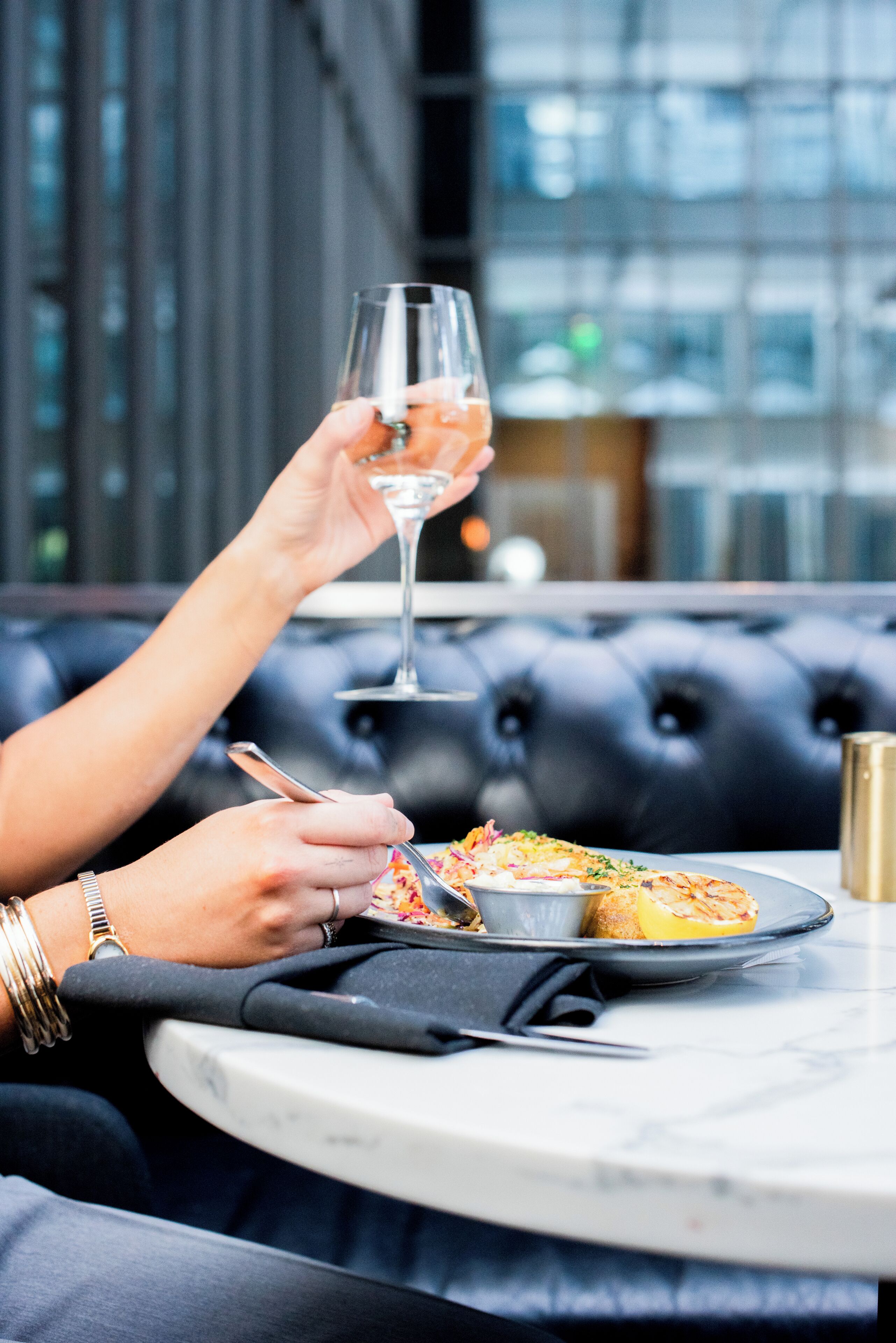 Una persona cenando en una mesa, con una copa de vino, un plato de comida y una taza dorada.