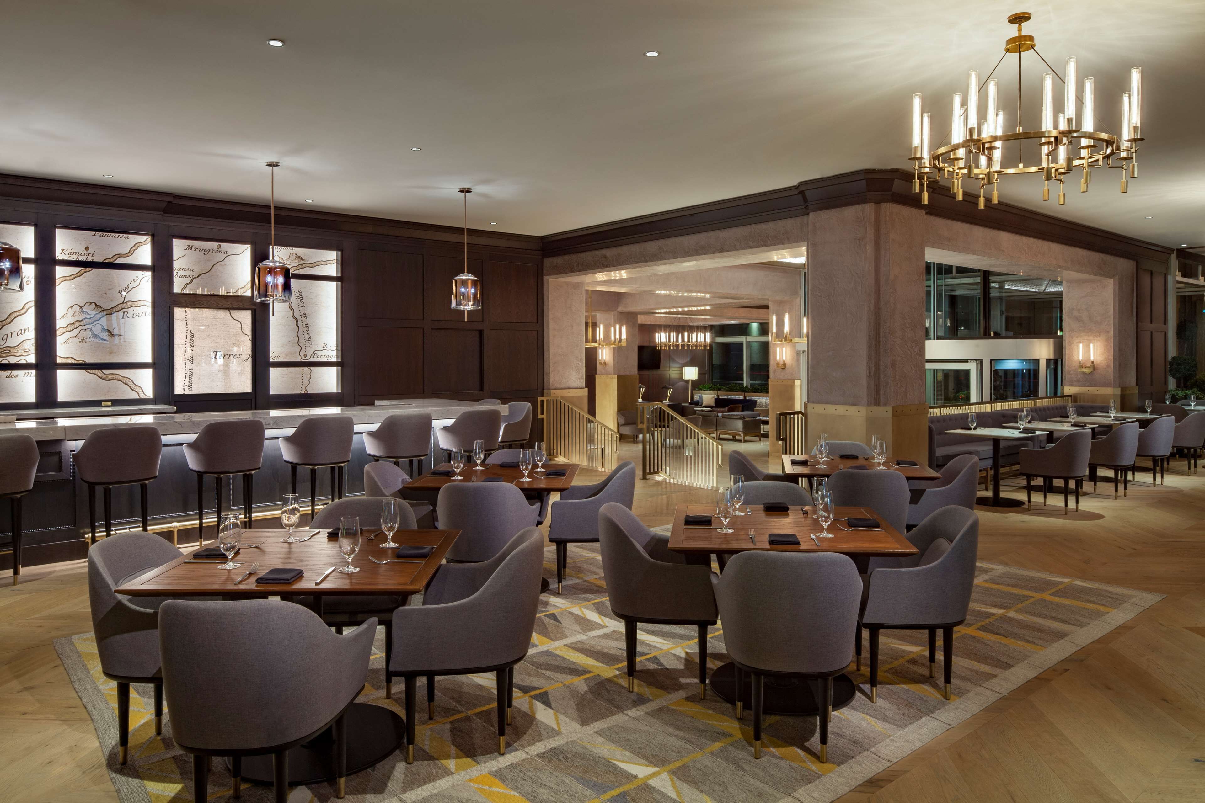 A spacious dining area with multiple tables and chairs, a chandelier, and a large window with a map design.