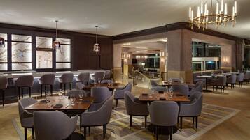 A spacious dining area with multiple tables and chairs, a chandelier, and a large window with a map design.