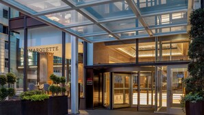 Een moderne hotelentree met een glazen gevel, een zichtbaar restaurantgedeelte en een goed verlicht interieur.
