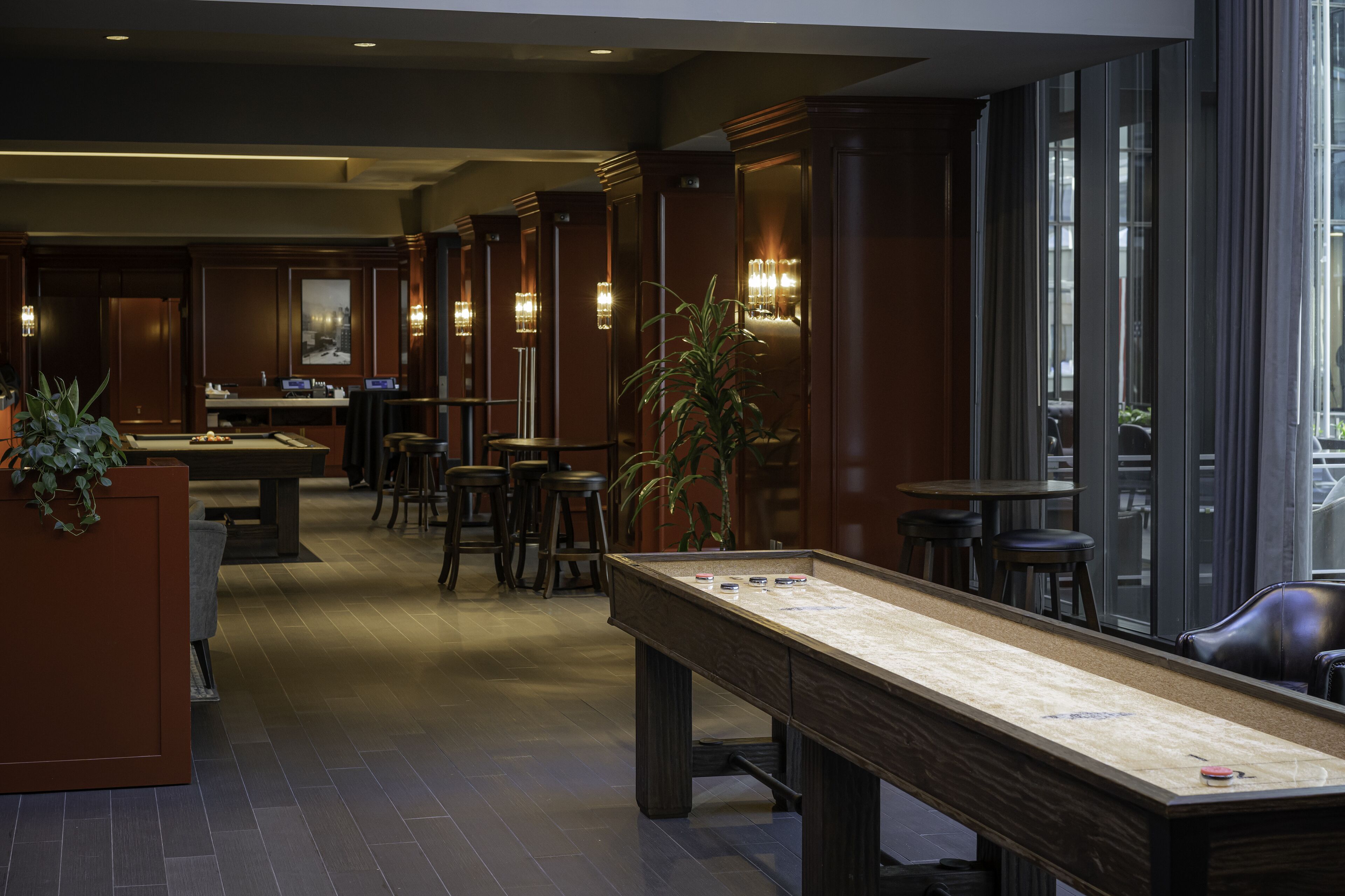 A billiards table in a dimly lit room with wooden paneling and bar stools.