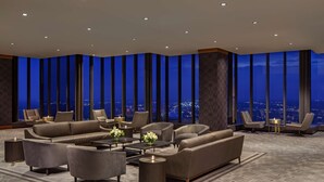 Een moderne lounge met een panoramisch stadsgezicht, leren banken en een vloerkleed met een patroon.