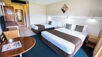 Habitación de hotel con dos camas, una mesita, un televisor y una lámpara fijada a la pared.