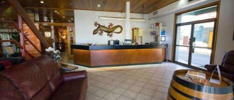 A hotel lobby with a reception desk, a leather sofa, a wooden bar, and a large window.
