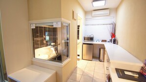 Um banheiro moderno com uma banheira em vidro, uma pia pequena e um micro-ondas na cozinheneta adjacente.