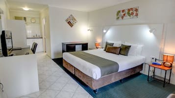 A hotel room with a large bed, a desk, a chair, a small kitchen area, and a bathroom.