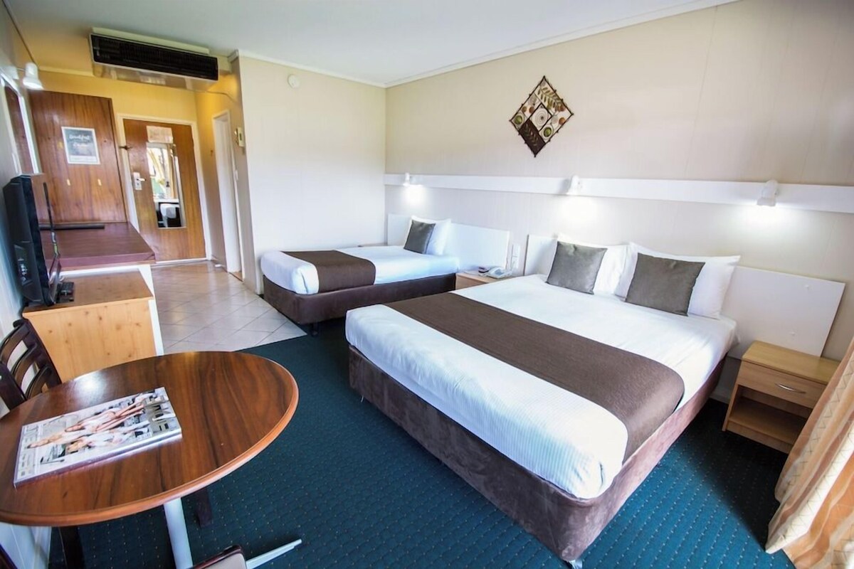 A hotel room with two beds, a small table, a TV, and a wall-mounted artwork.