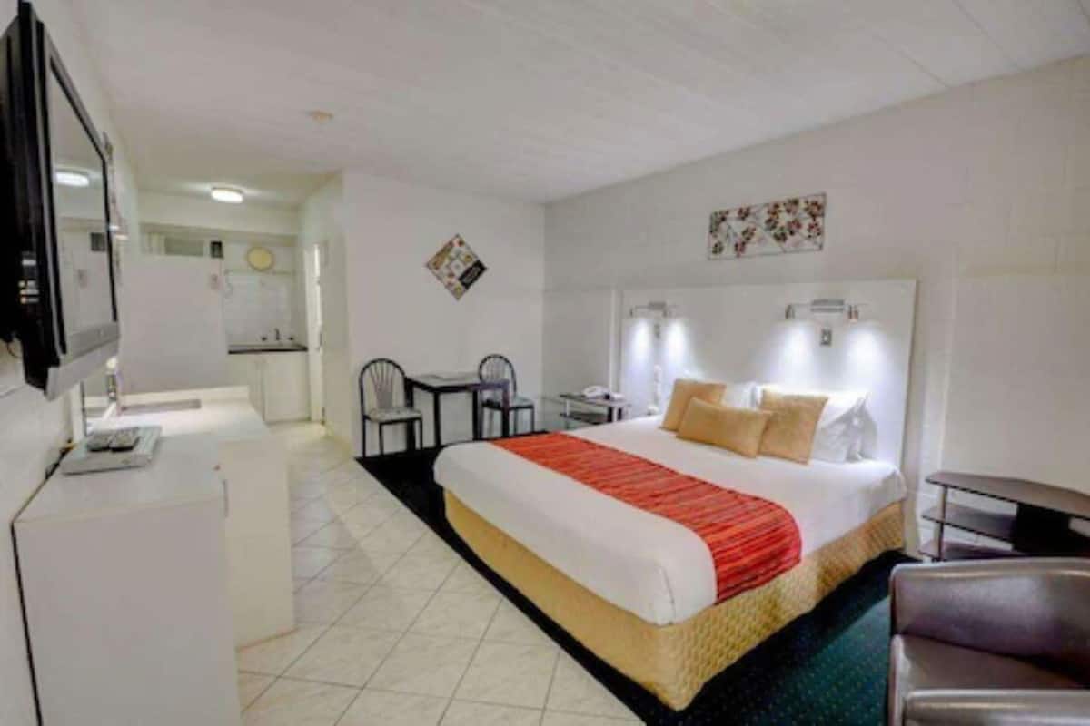 A hotel room with a bed, a desk, a chair, a television, and a bathroom visible in the background.