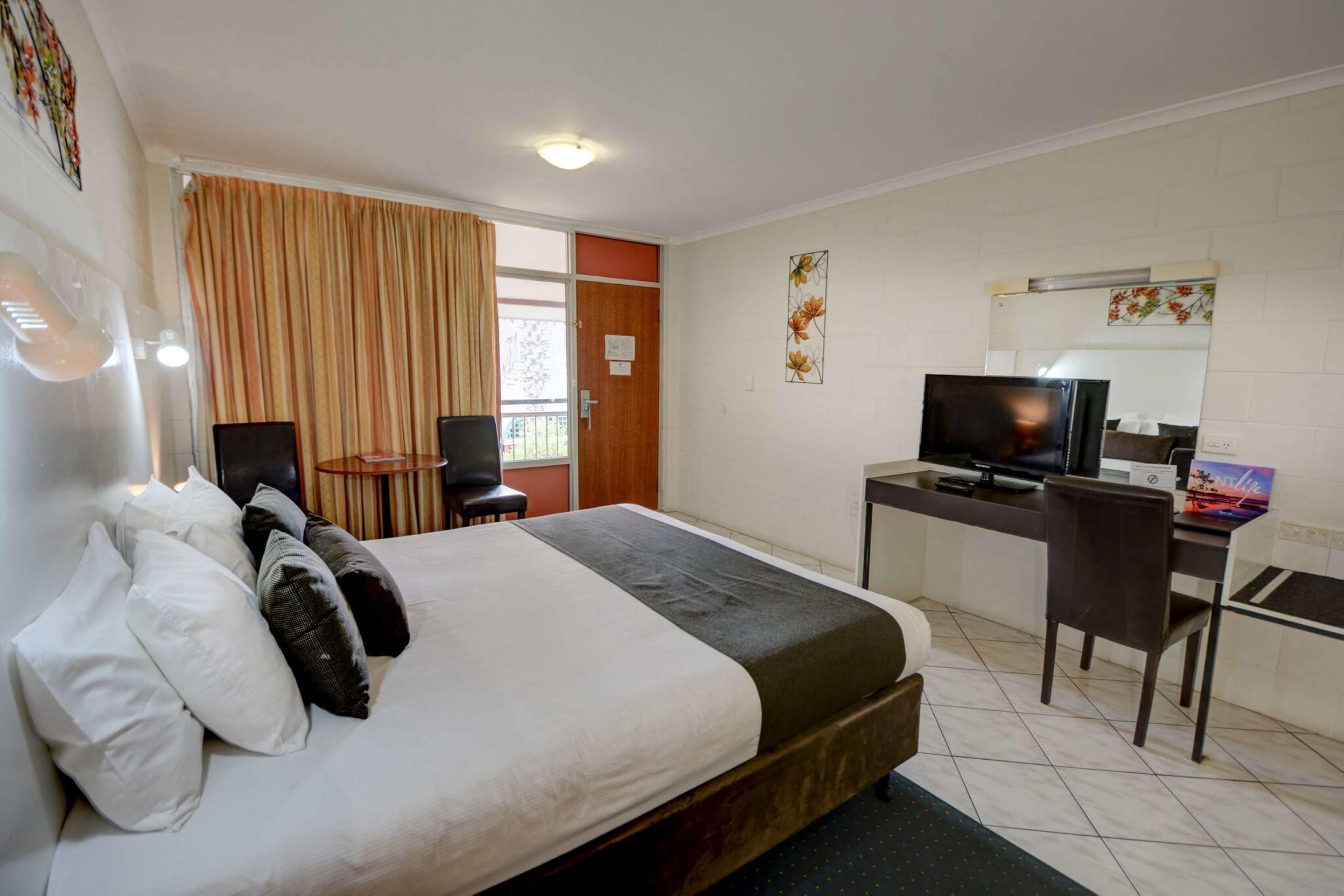 A hotel room with a bed, a desk with a computer and TV, a chair, and a window with curtains.