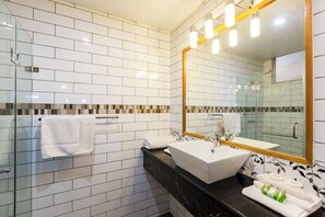A modern bathroom with white tiled walls, a black countertop, a white sink, and a large mirror with a gold frame.