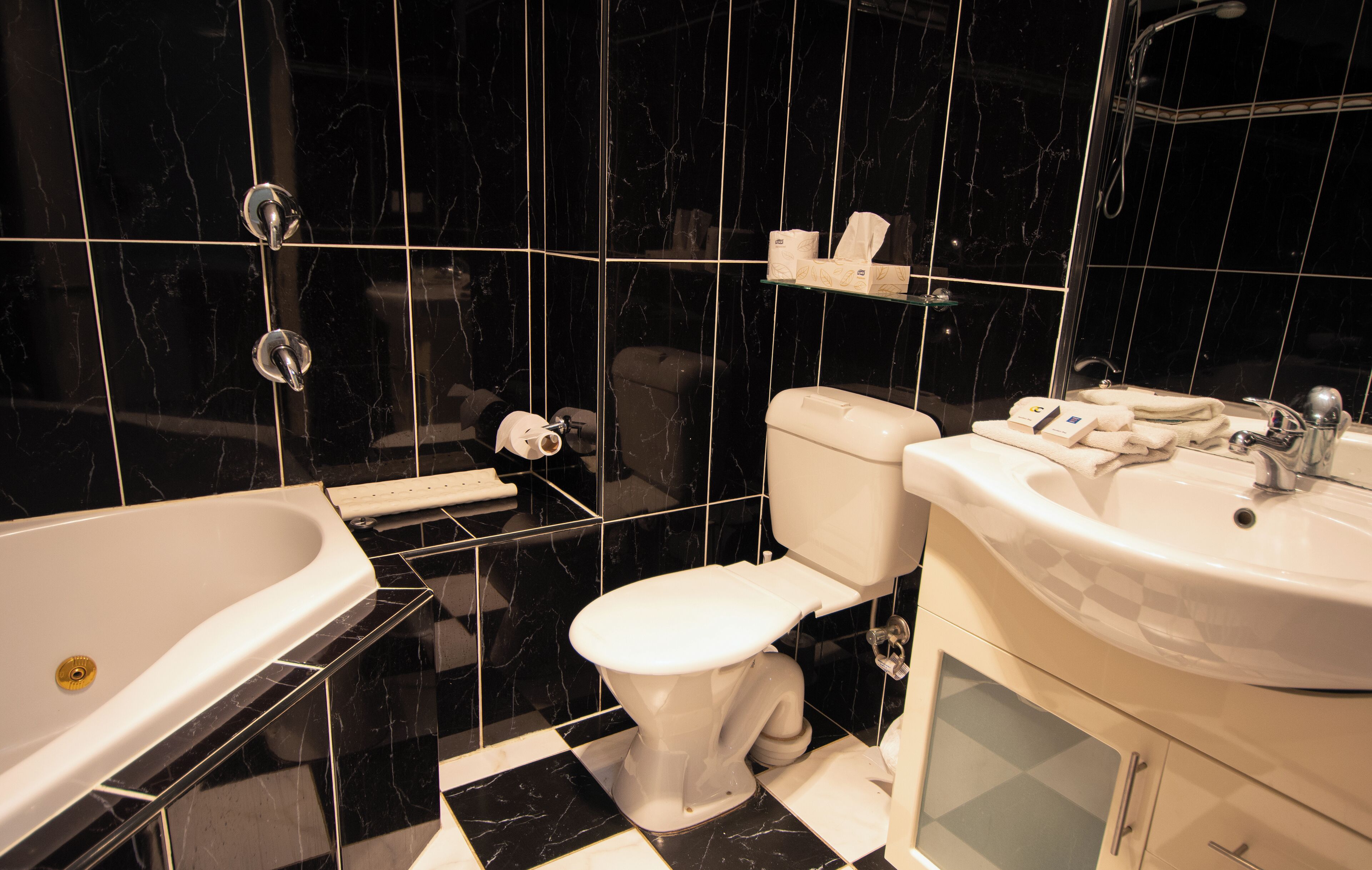 A modern bathroom with a black and white checkered floor, a white bathtub, a toilet, and a sink.