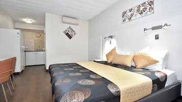 A bedroom with a bed, a desk, and a kitchenette.